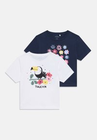 To t-skjorter med korte ermer: en hvit med en tukan grafikk og blomster, og en marineblå med fargerike blomster mønstre. Laget av bomull.