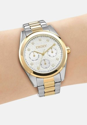 Orologio da polso DKNY in argento e oro con quadrante bianco, tre sottoquadranti per giorno, data e orario 24 ore, indossato al polso sinistro.