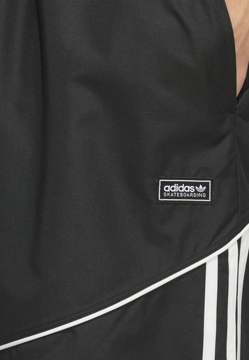 Short noir Adidas Skateboarding avec une bordure blanche et trois rayures verticales blanches sur la partie inférieure.