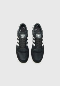 Chaussures de sport noires avec des rayures blanches, en suède et en mesh, bout rond et logo sur la languette. Les lacets sont marron foncé, avec une doublure intérieure à motif.