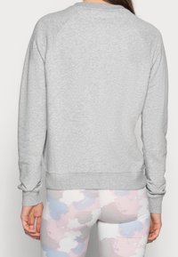 Woman wearing a light gray long-sleeve sweatshirt and pastel pink, blue, and white camouflage leggings, shown from the back.