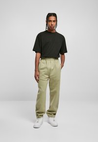 Black short-sleeve t-shirt paired with light olive-green sweatpants and white sneakers. The pants feature an elastic waistband and cuffs.