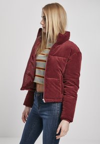 Burgunderfarget kordfløyelsjakke med høy krage, glidelås foran og frontlommeposter, med en blank rød lining. Brukt over en stripete grå crop top.