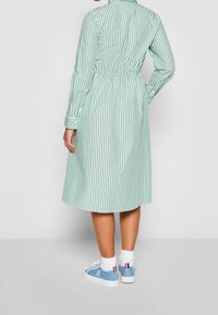 Vestito a righe verdi e bianche con maniche lunghe, vita stretta e lunghezza fino ai polpacci. Abbinato a sneakers blu e calzini bianchi.