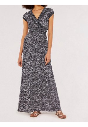 Femme portant une robe maxi noire à manches courtes avec motif floral, col en V, et des sandales plates blanches à brides.