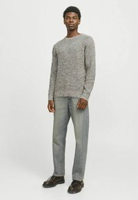 Suéter gris de punto con un acabado texturizado, combinado con pantalones vaqueros de mezclilla azul claro y zapatos negros de cordones. El estilo es casual y de corte relajado.