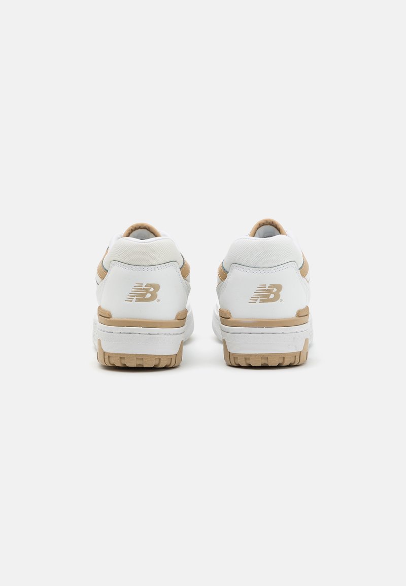 Une paire de baskets New Balance blanches et beiges montrées de l'arrière, mettant en valeur le logo sur le talon et les semelles en caoutchouc texturées.