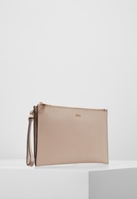 Béžová kožená psaníčko se strukturovaným povrchem, vybavená zlatým zipem a odnímatelným náramkem na zápěstí. Minimalistický design, obdélníkový tvar.