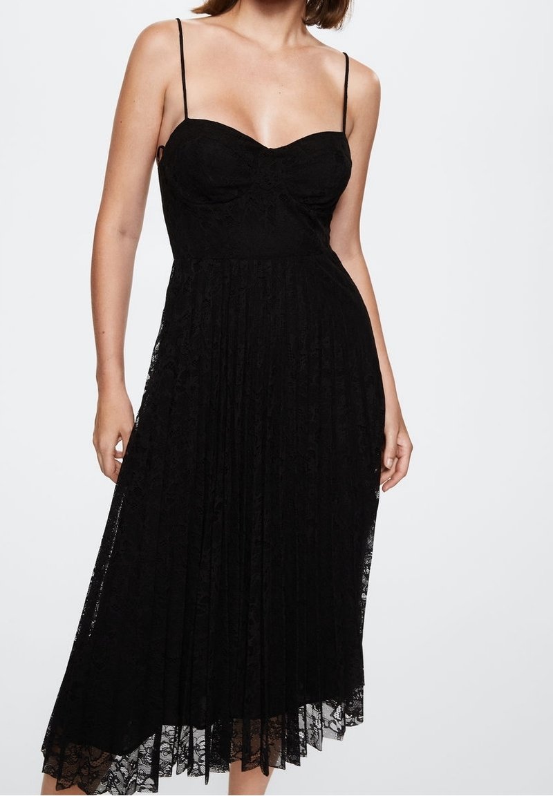 Černé krajkové šaty s tenkými ramínky, výstřihem do tvaru srdce a plisovanou sukní. Látka má květinový vzor a lemování, které sahá do poloviny lýtek.