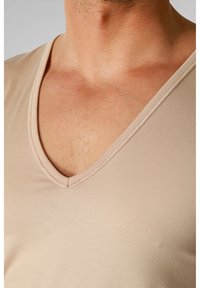 Beżowa koszulka z dekoltem w serek, wykonana z gładkiego materiału, charakteryzująca się prostym wzorem, z przeszytym dekoltem i miękką teksturą.