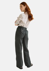 Pantalons en lin gris foncé avec une taille élastique, deux poches arrière et une coupe décontractée, associés à un haut léger à manches longues.