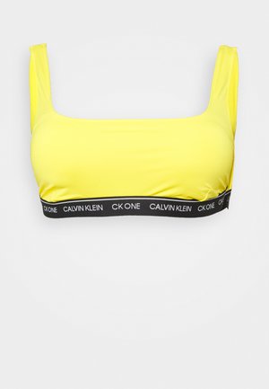 Bralette amarelo com decote quadrado e alças largas. Apresenta uma faixa elástica preta com a marca "CALVIN KLEIN". Textura suave.