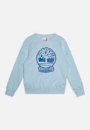 Világoskék pulóver kerek nyakkal, bordázott mandzsettákkal, és egy nagy kék Timberland fa logóval az elején. Puha anyagú textúra.