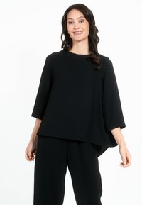 Top nero, dalla vestibilità ampia, con maniche tre quarti, scollo rotondo e orlo curvo. Tessuto liscio, abbinato a pantaloni neri.