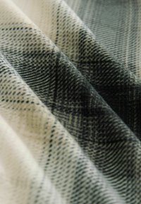 Tissu texturé présentant un motif à carreaux en crème et nuances de noir, avec des épaisseurs de ligne variées et un drapé doux.