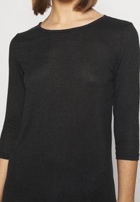 Top nero a maniche lunghe con scollatura rotonda, realizzato in tessuto a coste. Design aderente con una leggera texture e maniche orlate.