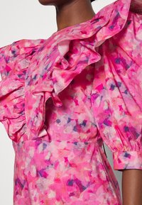 Robe florale rose avec épaules à volants, tissu texturé et couleurs vives mélangeant des tons de rose clair et foncé.