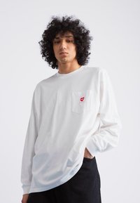 Long-sleeve white t-shirt made of cotton, featuring a small red heart design on the left chest pocket and a relaxed fit.