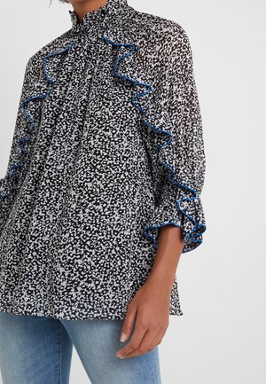 Schwarze und weiße Bluse mit floralem Muster und Rüschenbesatz, mit blauen Akzenten am Kragen und den Ärmeln, aus leichtem Stoff gefertigt.