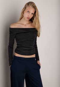 Top a righe nere e grigie scollato sulle spalle con maniche lunghe, design aderente e tessuto morbido, abbinato a pantaloni blu navy con coulisse.