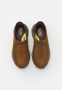 Pantofi slip-on din piele maro, cu laturi texturate, vârf rotund, interior căptușit și talpă din cauciuc. Prezintă branding-ul "Skechers Slip-Ins".