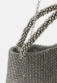 Beaded kabelka s kovovým stříbrným povrchem, nabízející strukturovaný tvar a dvojité texturované popruhy zdobené reflektivními korálky.