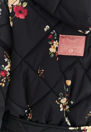 Czarna pikowana tkanina z drobnym kwiatowym wzorem oraz różowa naszywka z ilustracją oka i częściowo czytelnym tekstem.