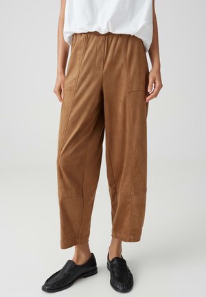 Pantalon court marron taille haute avec coutures frontales et poches, porté avec des chaussures noires sans lacets et un haut blanc rentré.