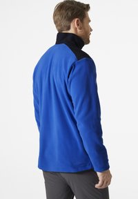 Blauer Fleece-Pullover mit schwarzem Kragen. Weiche Textur, lockere Passform, lange Ärmel und gesäumter Saum. Entworfen für Komfort und Wärme.