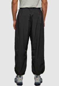 Černé lehké kalhoty s elastickým pasem, volným střihem a manžetami u kotníků. Mají zadní kapsu a šňůrkové detaily.