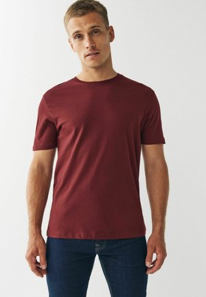 Bordeaux korthandig T-shirt in een zachte, gladde stof met een ronde halslijn. Strak design, gecombineerd met donkerblauwe jeans. Minimalistische stijl.