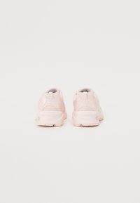 Baskets de sport rose clair avec des panneaux en mesh, forme arrondie, semelles rembourrées et accents texturés. Le design comporte une languette au talon.