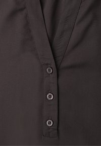 Gros plan sur le devant d'une chemise noire avec trois boutons visibles et une couture d'encolure en forme de V.