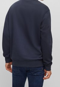Mörkblå sweatshirt med rundad halsringning, ribbade ärmar och nederkant. Slät textur med minimala detaljer, bärs med mörkblå jeans.