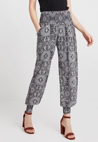 Black and white patterned trousers with a smocked waistband, side pockets, and tapered cuffs, paired with block-heeled sandals.