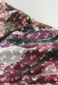 Gros plan d'un tissu texturé multicolore avec des nuances de rose, vert, brun et blanc et des boutons recouverts de tissu le long d'une couture.