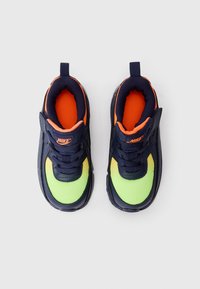 Pár modro-navy a neónovo zelených Nike tenisky s oranžovým vnútorným podšívkou a šnurovacím dizajnom, zobrazené zhora na neutrálnom pozadí.