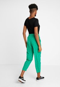 Green trousers with black polka dots, elastic waistband, and cropped design. Paired with a black short-sleeve top and black sneakers.