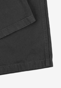 Czarna bawełniana tkanina o teksturowanym wykończeniu, z zagiętymi brzegami i starannym ściegiem, prezentująca wytrzymałość i schludny design.