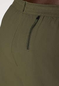Shorts vert olive avec une ceinture élastique, dotés d'une poche zippée et d'un tissu texturé avec un motif subtil.