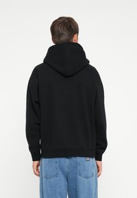 Sort hættetrøje med en stor, tyk hætte, blød tekstur og løs pasform, parret med lyseblå denim jeans med en lomme bagpå.