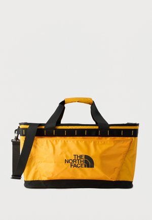 Geel-zwarte rechthoekige reistas met zwarte handvatten, verstelbare schouderriem en het logo van "The North Face" middenvoor.