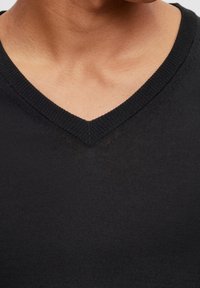 Černé tričko s výstřihem do V vyrobené z měkké bavlny, s texturovanou pleteninou a hladkým zakončením kolem výstřihu.