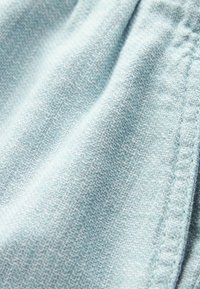 Svetle modrý látkový materiál s jemnou geometrickou texturou, který se vyznačuje měkkým, tkaným vzhledem a viditelným šitým okrajem.