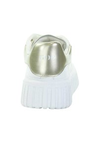 Białe sneakersy z grubą żebrowaną podeszwą i metalicznym złotym akcentem na pięcie, z częściowo odblaskowym tekstem.