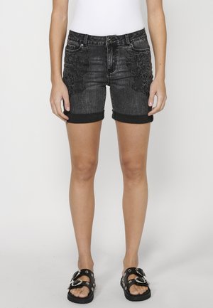 Shorts en denim noir avec broderie florale sur le devant, ourlet roulé et design à cinq poches. Associés à des sandales noires avec des accents métalliques.