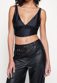 Černý saténový crop top s hlubokým výstřihem do V, na přední straně s nařasením a širokými ramínky, kombinovaný s černými koženými kalhotami s vysokým pasem.