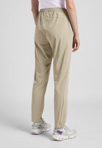 Lichtbeige joggers met elastische tailleband en taps toelopende boorden. Glad textuur en minimale stiksels. Achterkant heeft "TEXSHIELD" branding.