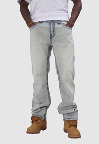 Jasnoniebieskie spodnie dżinsowe z kontrastującymi ciemnymi szwami, luźny krój i kieszenie boczne, w połączeniu z brązowymi butami roboczymi.