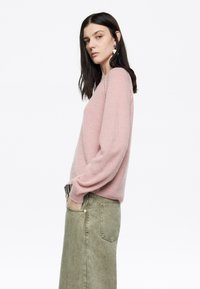 Maglione lavorato a maglia rosa chiaro con una vestibilità comoda, maniche lunghe e polsini a coste. Abbinato a una lunga gonna di jeans verde oliva.